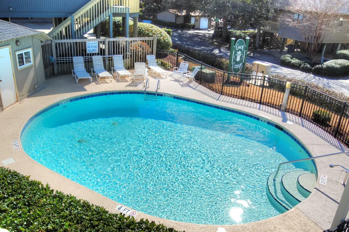 The image showcases a sparkling swimming pool surrounded by comfortable lounge chairs and lush greenery, with inviting poolside steps leading into the water. The setting suggests a tranquil atmosphere perfect for both relaxation and social gatherings, and hints at memorable activities like sunset swims and poolside barbecues.