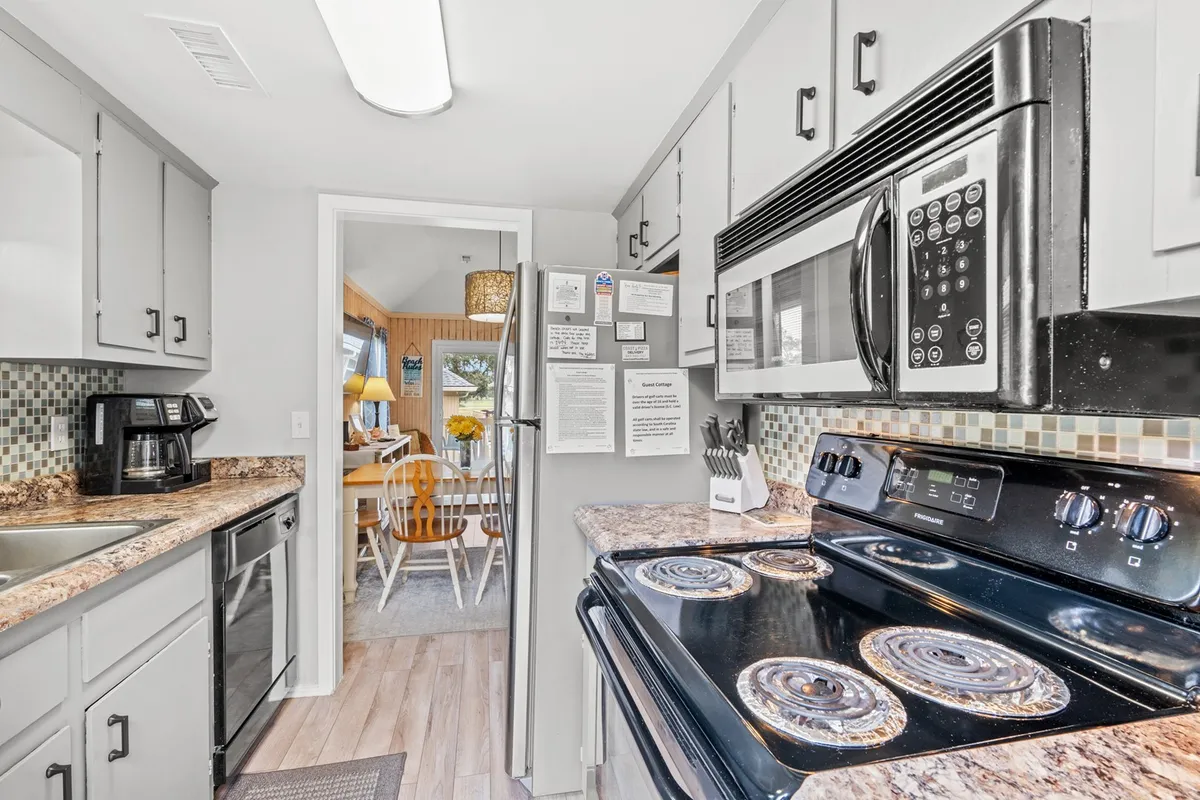 A spacious, modern kitchen featuring sleek appliances, granite countertops, a colorful tile backsplash, and a wooden dining table visible in the background. The space is well-lit and inviting, ideal for both cooking and socializing with family and friends.