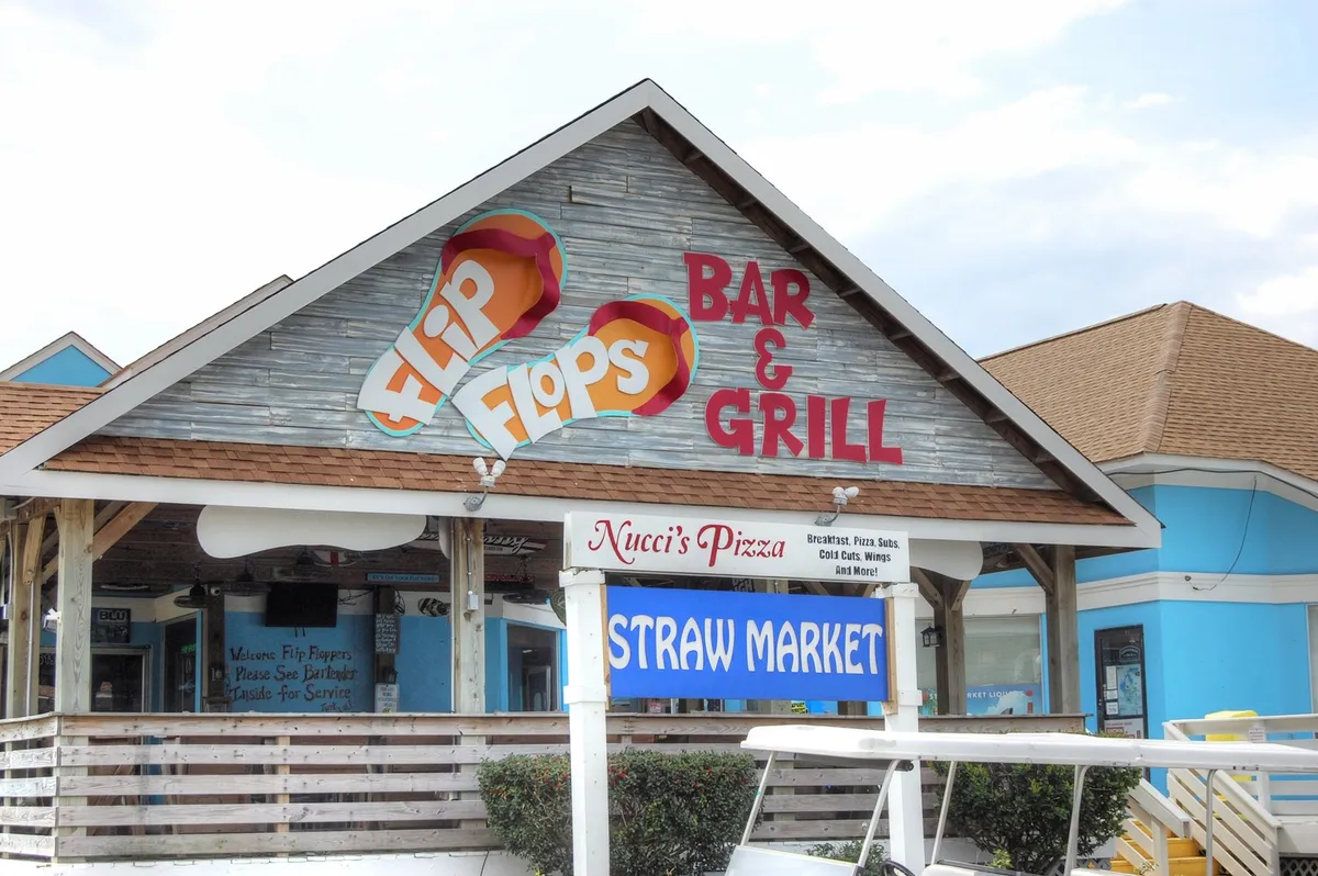 A colorful exterior shot of local restaurants and bars, including Flip Flops Bar & Grill and Nucci's Pizza, with signage and outdoor seating creating a lively, welcoming atmosphere.