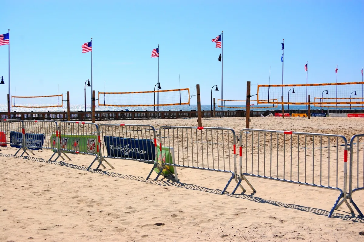 A lively beach scene with volleyball nets set up on the sand, American flags fluttering, and people enjoying various beach activities. The scene is energetic and social, reflecting the fun, active beach lifestyle Myrtle Beach is known for.