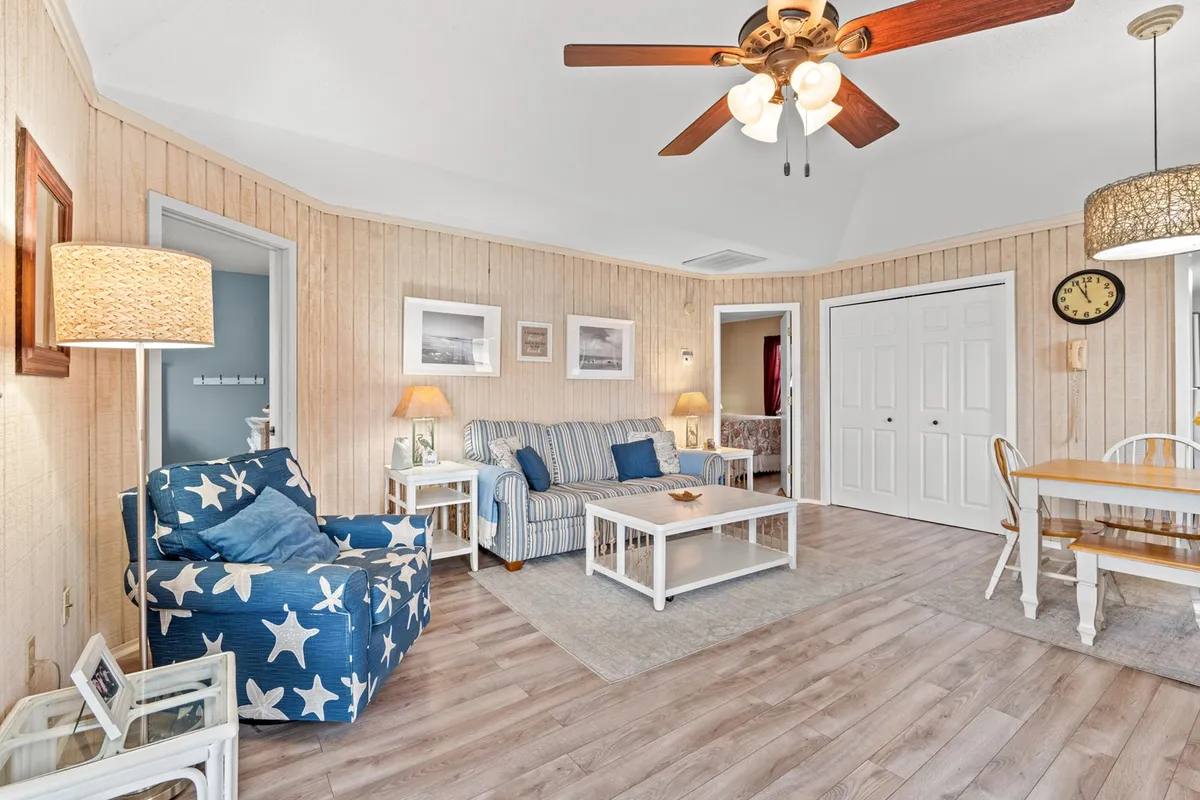 This image highlights a comfortable living area with a striped sofa, star-patterned chair, and a dining table beneath stylish light fixtures. The decor is cheerful and homely, and the whole setting is bathed in soft, inviting light. The arrangement is perfect for socializing, family dinners, or quiet reading sessions.