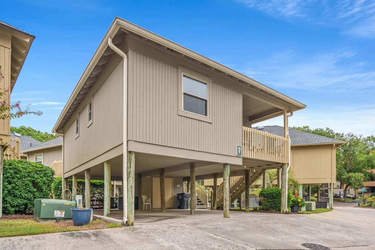 An exterior view of the cottage, highlighting the elevated structure with under-house parking, a welcoming porch area above, and lush greenery surrounding the property. The scene gives a sense of security, comfort, and the seamless blend of private and shared spaces.