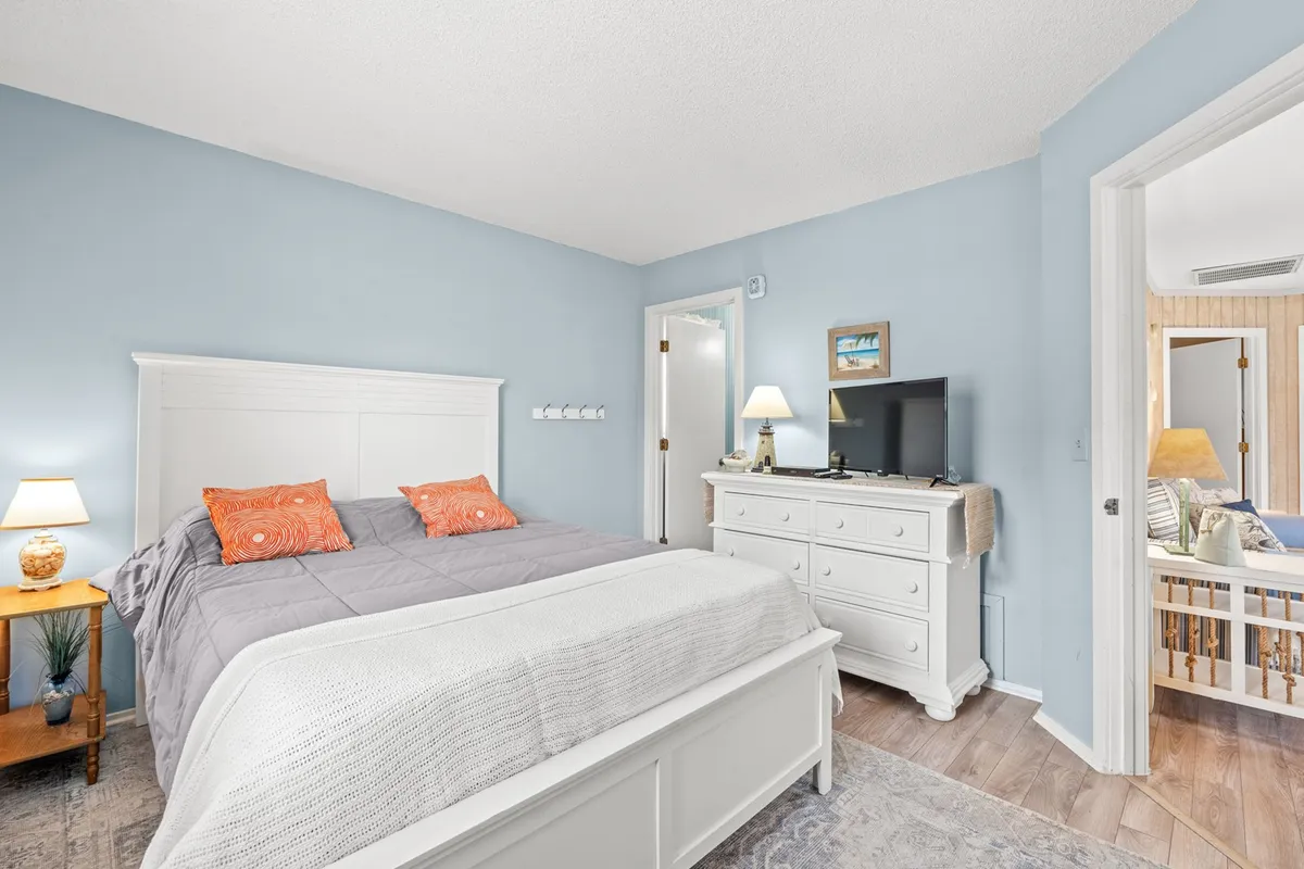 A comfortable bedroom with a bed, dresser, nightstand, and a television. Natural light pours into the space, and the setting is perfect for relaxing, watching TV, or reading. The room looks warm, clean, and ready for guests of all ages.