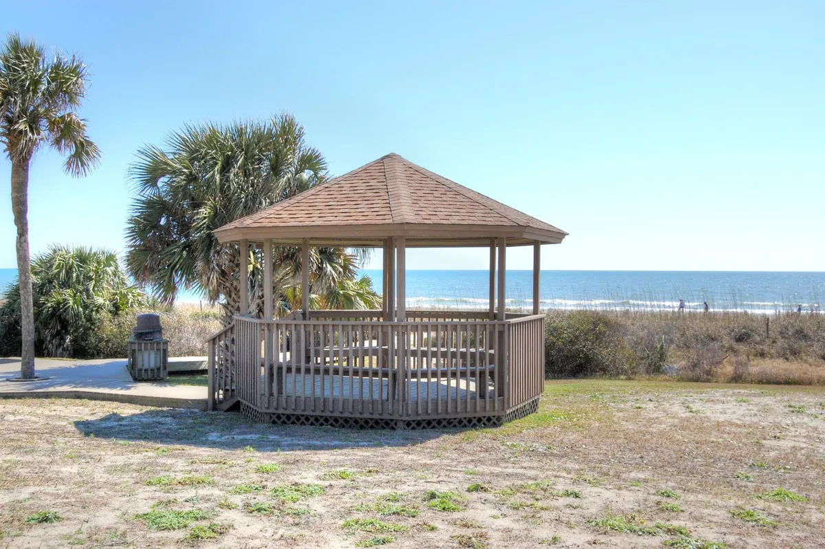 A serene exterior shot featuring a charming gazebo overlooking the ocean, surrounded by lush palm trees. The waves roll gently in the background, creating a peaceful and inviting coastal scene ideal for relaxation or social gatherings.